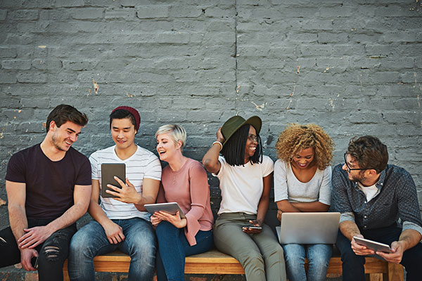 six young people looking at phones, tablets and laptops