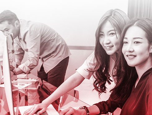 smiling Asian workers at a table with laptops