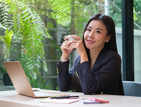 smiling Asian woman sitting at a table holding a cup