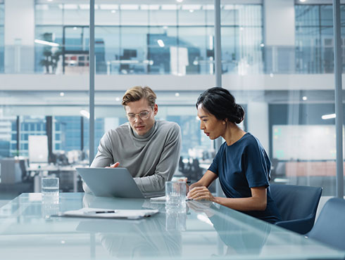 Man and woman sitting in a conference room look at a laptop