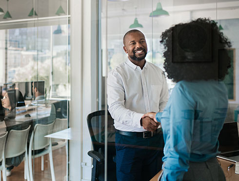 smiling man in white shirt shaking hands with woman in blue in an office