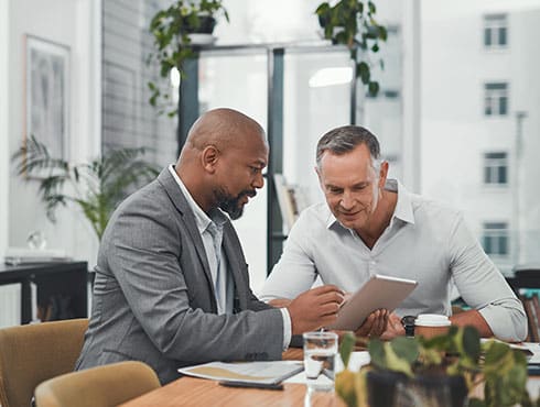 two men in an office seated at a table looking at a pad of paper