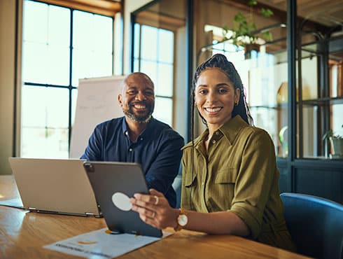 two smiling people sitting at a desk with a laptop computers
