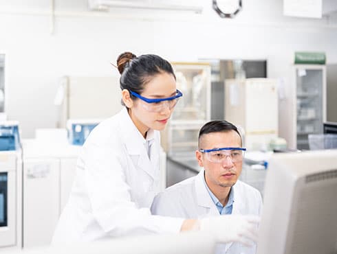 two people in lab coats looking at a computer screen